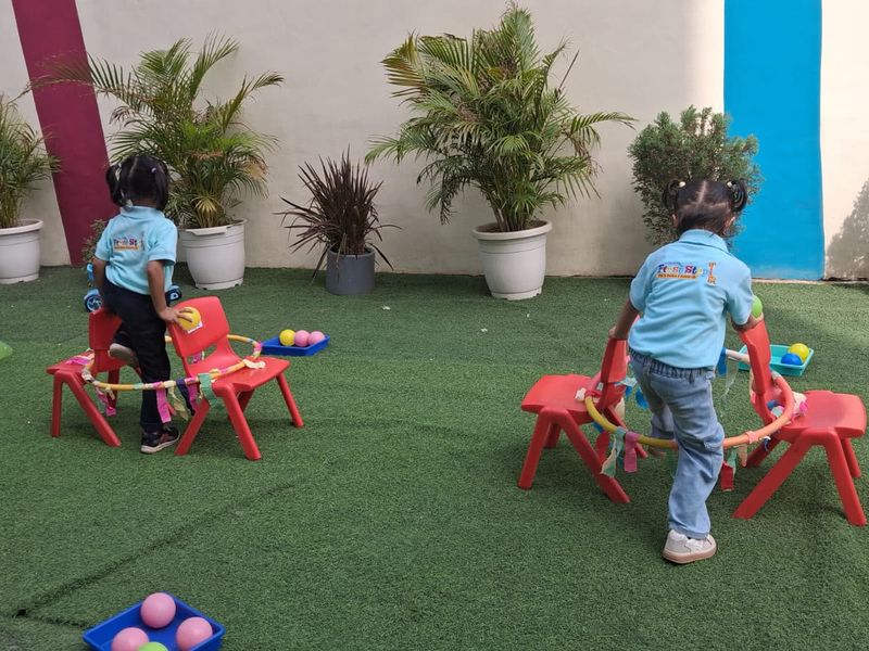 Toddlers moving between chairs and balls on the outdoor turf