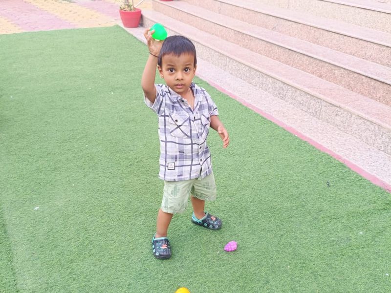A toddler playing with balls on the outdoor turf beside the garden steps