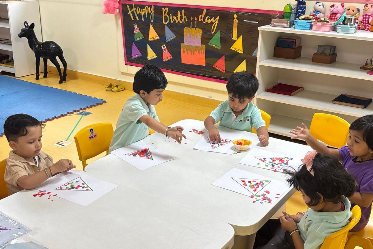 Preschoolers sitting together at a low table doing a paper-dot art activity