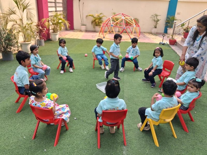 Children sitting in a circle on small chairs for a group game on the outdoor turf