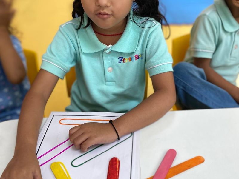 A Nursery child arranging coloured craft sticks to match a pattern card