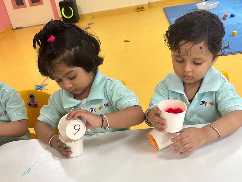 Two toddlers exploring paper cups and paint at a low table in Play Group